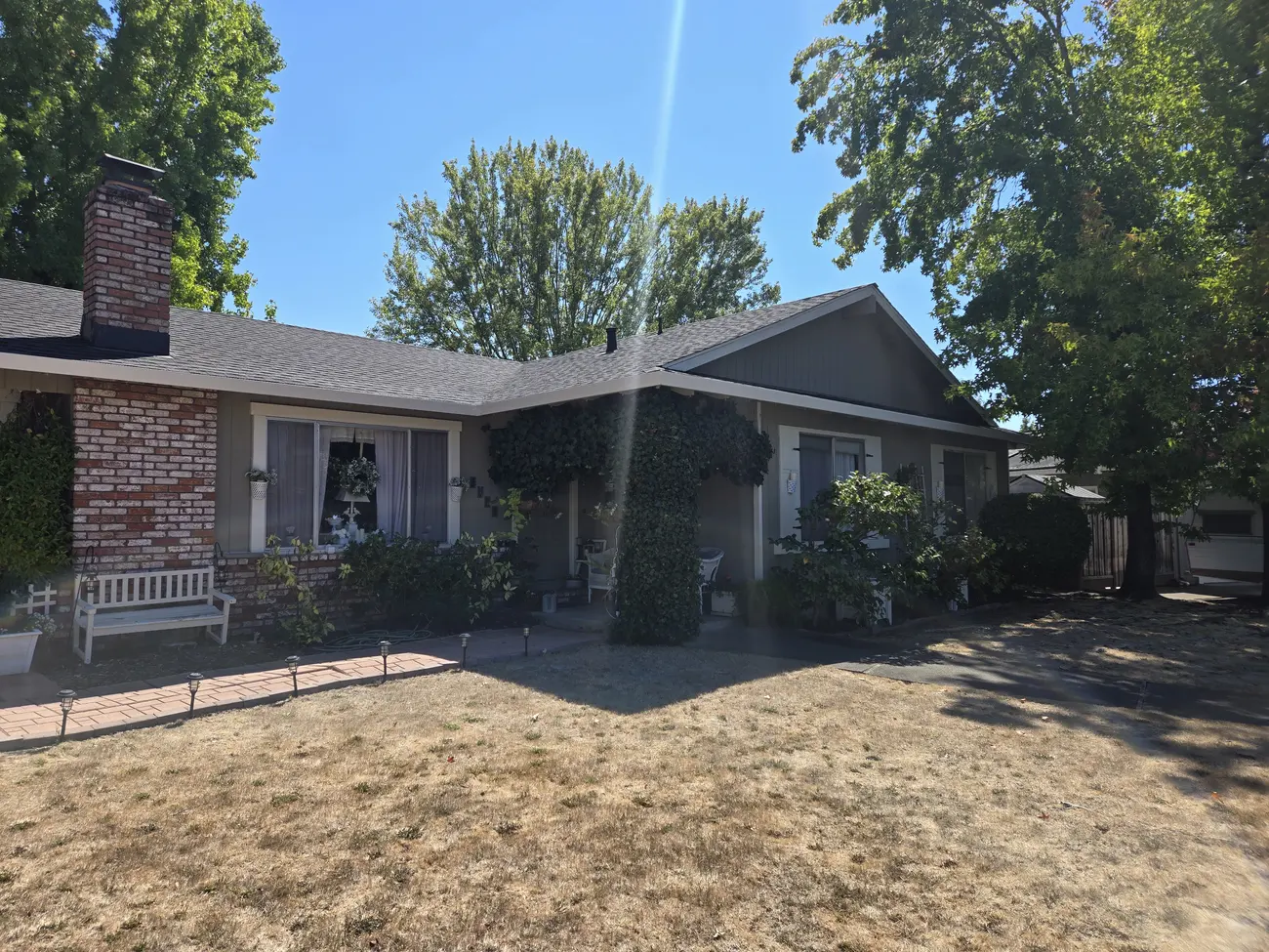Brick ranch house with ivy climbing the porch wall and a dry lawn